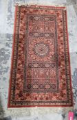 Eastern red ground rug with central floral medallion flanked by geometric pattern with multiple