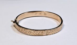9ct gold hinged bangle with safety chain, one half engraved, the other plain, 6cm wide, 8.5g