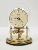 German ' Kundo ' small gilt anniversary clock with glass dome, the backplate stamped Kieninger &