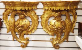 Pair of giltwood wall brackets of shaped demi-lune form, each carved with foliate scrolls, a bird