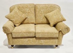 Modern two-seater sofa upholstered in a yellow fabric, on turned wooden legs with brass castors,