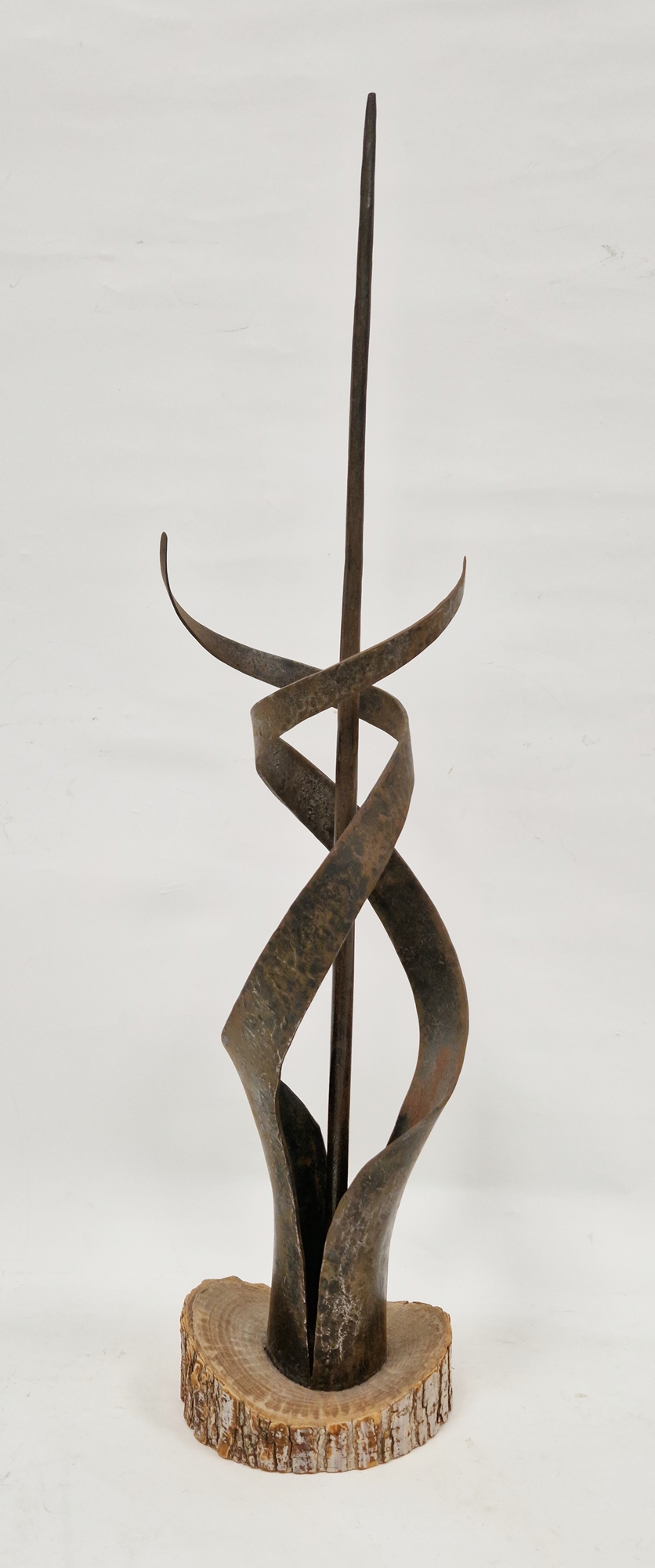 An abstract metal sculpture of spiral form surrounding central pillar, mounted on a wooden base,