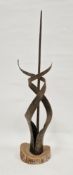 An abstract metal sculpture of spiral form surrounding central pillar, mounted on a wooden base,