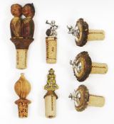 Seven novelty cork bottle stoppers including silver topped stopper in the form of a Bacchus on a