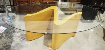 Tom Schneider Wave dining table, the oval glass top on an S-scroll pale oak plinth base, 77cm high x