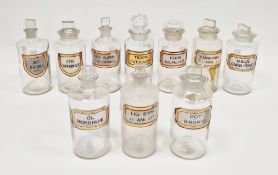 Ten early 20th century 'label under glass' apothecary bottles and stoppers, each of cylindrical form