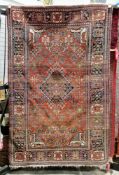 Persian style red ground wool rug, decorated with a central medallion surrounded by stylised flowers