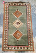 Green and cream wool rug, decorated with three medallions within a stylised geometric border,