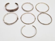 Three silver hinged bangles with engraved decoration together with two silver torque bangles,