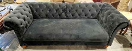 Chesterfield sofa upholstered in a dark teal velveteen fabric with button backs and arms, on