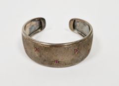 White metal torque bangle with engine turned finish, illusion set with five small rubies, 6cm