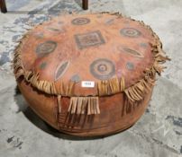 Mid-century ethnic leather pouffe of circular form, the top with geometric decoration and fringe,