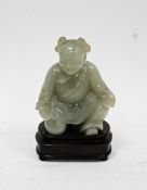 Chinese carved pale celadon jade model of a kneeling boy on wooden stand, Qing Dynasty, with his