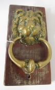 Antique brass lion door knocker, the lion mask mounted on wooden plaque, the plaque 28cm x 14cm