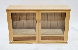 Modern pale mixed wood hanging wall cabinet with twin part glazed doors opening to a glass shelf and
