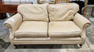 Modern cream upholstered two seater sofa, with scroll arms, on turned tapering front legs with brass