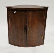 George III oak bow-front hanging corner cabinet, the two panel doors opening to a painted interior
