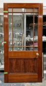 Large hardwood door with glass panel surrounded by eight smaller glass panels, with brass knob