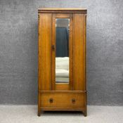 An early 20th century oak wardrobe having a carved frieze over a single mirrored door flanked by