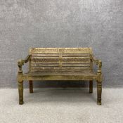 A weathered Chic Teak garden bench having a carved top rail and back over two scrolling arms and a