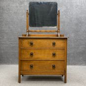 An early 20th century oak dressing chest having a rectangular swing mirror on carved supports