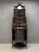 An Edwardian mahogany corner cabinet in two parts having a carved cresting above a shaped pediment