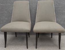 A pair of mid-century dining chairs upholstered in grey fabric with a white trim on ebonised round