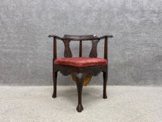 A Georgian mahogany corner chair with a carved top rail and shaped armrests terminating in scrolling