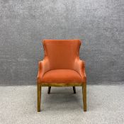A mid century stained pine wingback armchair upholstered in a rusty orange velvet to the back arms