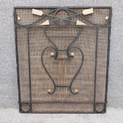 An early 20th century wrought iron fire guard having a shaped pediment with overlapping arrows