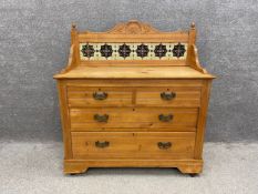 A late 19th century pine chest of drawers having a raised, shaped and carved tiled back on a pine