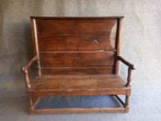 An 18th century oak settle with a tall panelled back flanked by fluted stiles with carved arms on