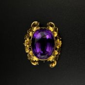 An amethyst brooch with a central cut cabochon stone set into a floral Rococo style yellow metal