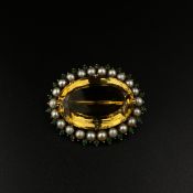 A Victorian oval citrine brooch with borders of pearls and emerald coloured stones set into a yellow