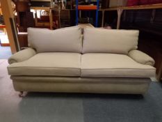 A contemporary Howard style sofa with scrolled arms raised on turned tapering mahogany supports