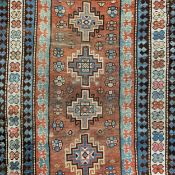 An early 20th century Kazak carpet having four geometric lozenge medallions over an abrash rust