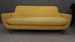A 1960's vintage style three seater sofa of stylish curvilinear form, upholstered in yellow fabric