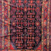 A Hamedan carpet having a repeating geometric pattern in iron red over a midnight ground