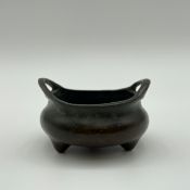 A Chinese patinated bronze twin handled tripod censer of squat ovoid form cast with six character