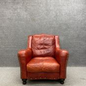 A vintage library armchair with a shaped back and arms in burgundy upholstery with brass stud-work