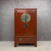 An early 20th century red lacquered Chinese wedding cabinet having two brass mounted doors opening