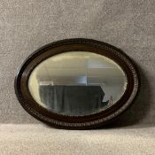 An Edwardian mahogany wall mirror with an egg and dart moulded oval frame around the original