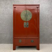 An early 20th century red lacquered Chinese wedding cabinet having two brass mounted doors opening