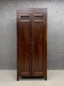 A 20th century Eastern hardwood wardrobe having a pair of carved panelled doors opening on to an
