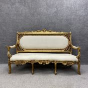 A Louis XVI style gilt salon sofa having a scrolled cresting above an openwork and upholstered