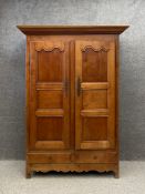 A 19th century French cherrywood armoire having a moulded cornice with two shaped panel doors over