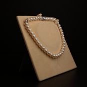 A 20th century pearl necklace with a spherical diamond encrusted polished metal clasp in a fitted