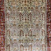 A silk Persian rug having a repeating foliate design over a biscuit ground surrounded by a border of