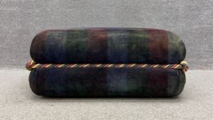 A contemporary footrest upholstered in a tartan chenille bound by a multicoloured rope knotted at