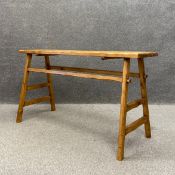 A 20th century pine trestle table having a narrow plank top with a carved edge raised on mortis